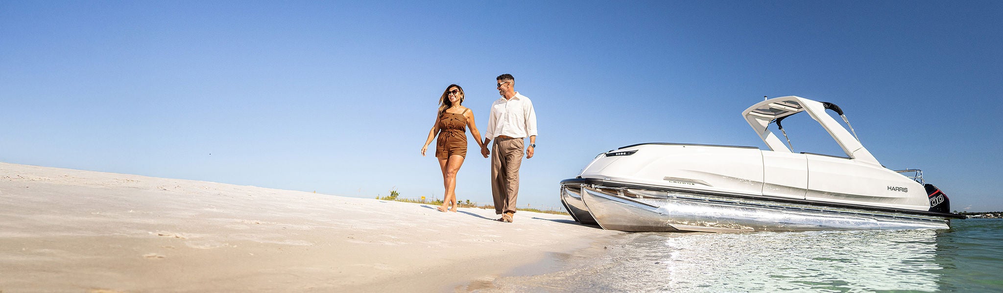 Man and woman walking on beach with Harris pontoon