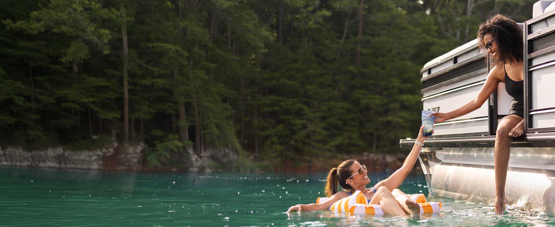 Two women sharing a drink while floating next to a Harris Solstice 250