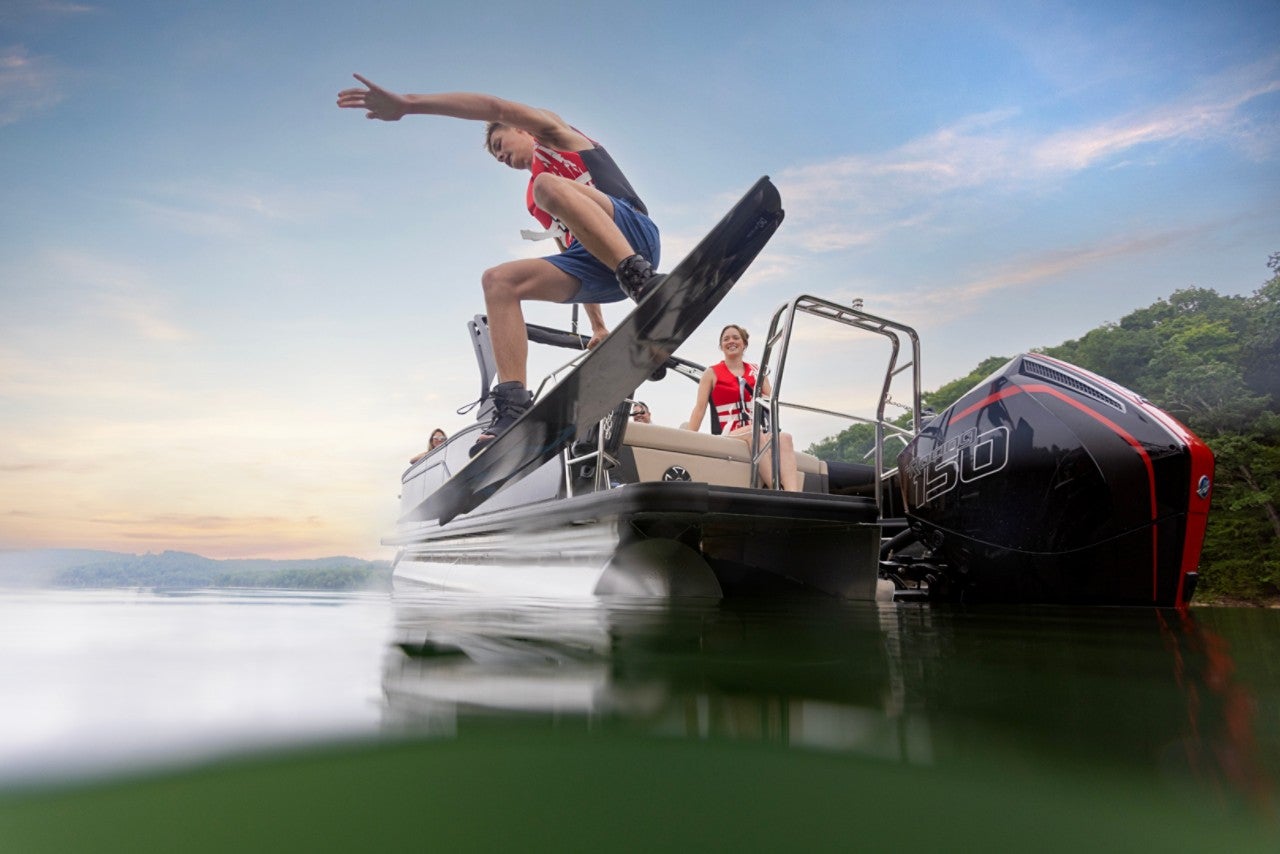 Teenage boy jumping off the back of a Harris pontoon boat into the water to wakeboard with his family. 